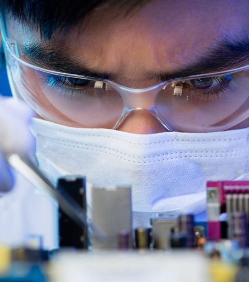 Close-up image of an engineer concentrated on electronic assembling on the foreground